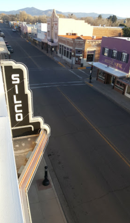 View of a quiet street with historic buildings and a theater sign, under clear skies and distant mountains.