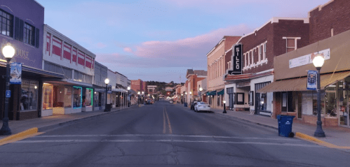 A quiet street lined with shops and lampposts, under a pastel sky at dusk.