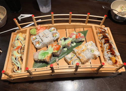 A wooden sushi platter featuring various sushi rolls, garnished with wasabi and sauces, on a dark table.