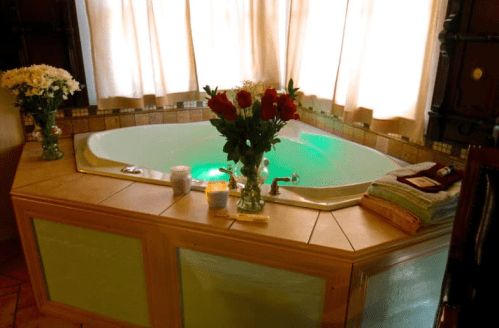 A cozy bathroom with a jetted tub, green lighting, flowers, candles, and neatly folded towels.