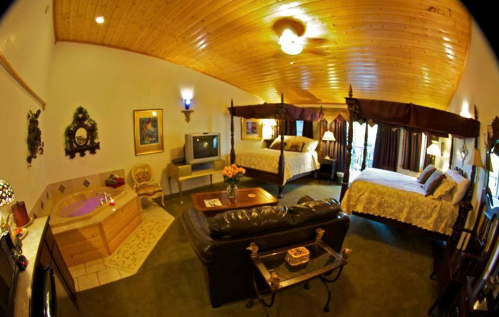 Cozy hotel room with two canopy beds, a sitting area, and a jacuzzi, featuring warm wooden accents and soft lighting.