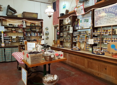 A cozy market interior with wooden shelves filled with jars, a table with ingredients, and vintage decor.