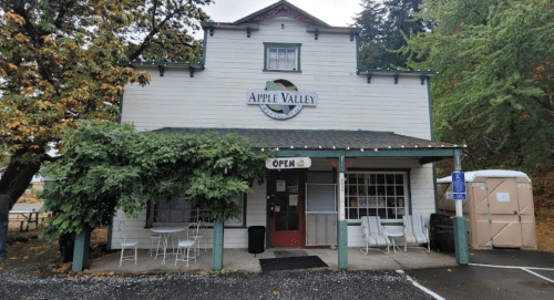 A quaint building with "Apple Valley" sign, surrounded by trees, featuring outdoor seating and an "Open" sign.