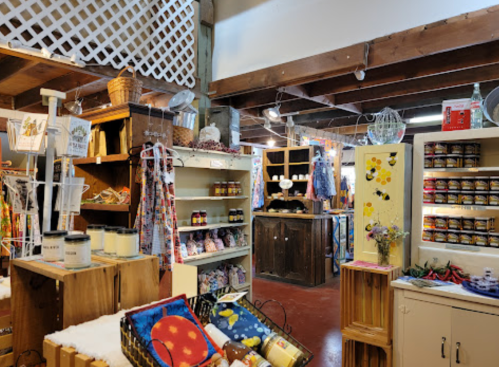 A cozy market interior with wooden shelves, jars of preserves, and colorful crafts displayed in a rustic setting.