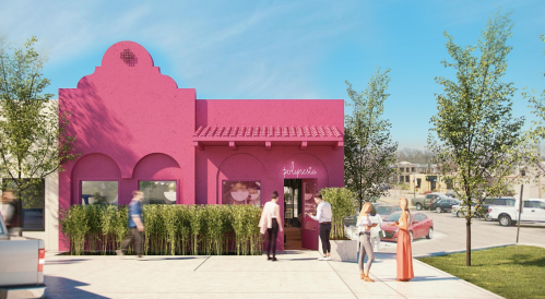 A vibrant pink building with a decorative roof, featuring people outside and greenery along the entrance.