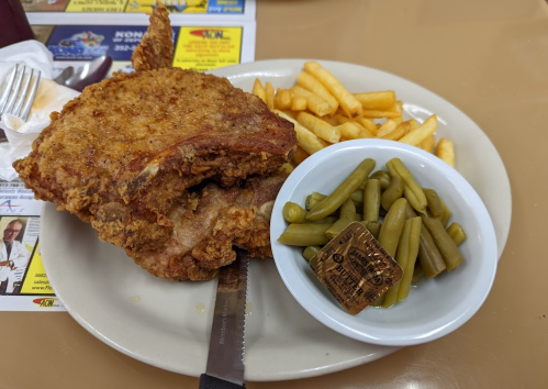 A plate with fried chicken, French fries, and a small bowl of green beans, accompanied by a butter packet.
