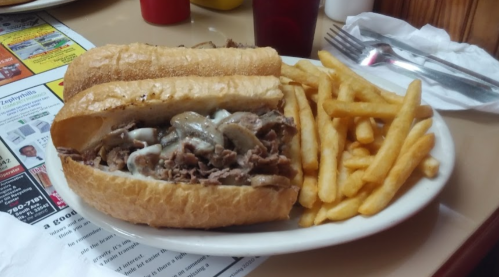 A plate featuring a large sandwich filled with beef and mushrooms, accompanied by a side of golden French fries.