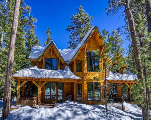 A beautiful wooden cabin surrounded by snow-covered trees under a clear blue sky.