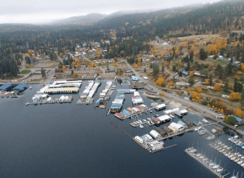 Aerial view of a marina with boats, surrounded by trees and buildings in a scenic, autumn landscape.