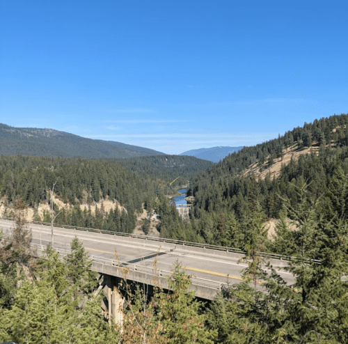 A scenic view of a highway winding through lush green forests and mountains under a clear blue sky.