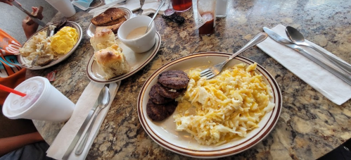 A breakfast spread featuring scrambled eggs, sausage patties, biscuits, and pancakes on a table with drinks.