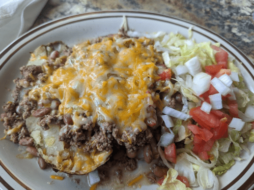 A plate of nachos topped with ground beef, melted cheese, and served with lettuce, tomatoes, and onions on the side.