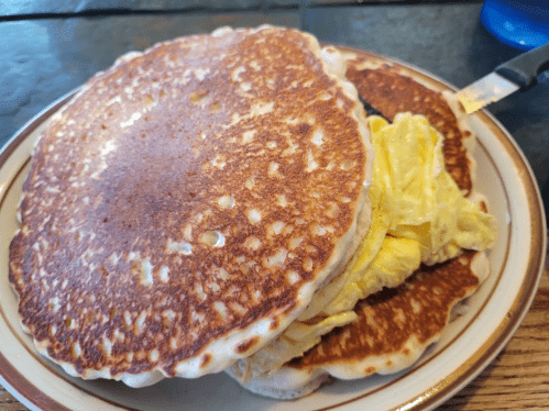 A stack of golden-brown pancakes with scrambled eggs in between, served on a plate.