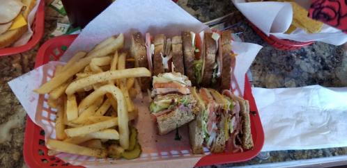 A basket with a club sandwich stacked high, accompanied by a side of seasoned French fries and pickles.