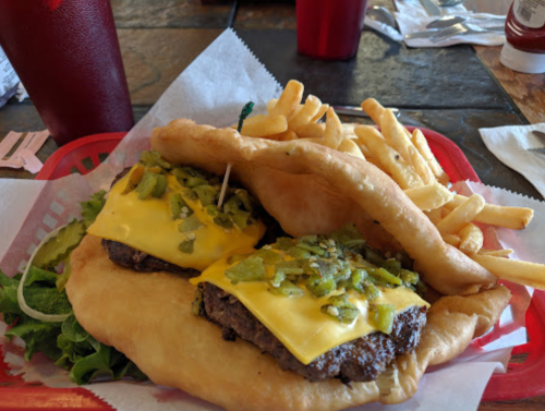A plate featuring two cheeseburgers topped with green peppers on a fried bun, served with fries and a side salad.