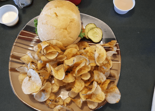 A plate with a sandwich, lettuce, a pickle slice, and a generous serving of crispy potato chips.