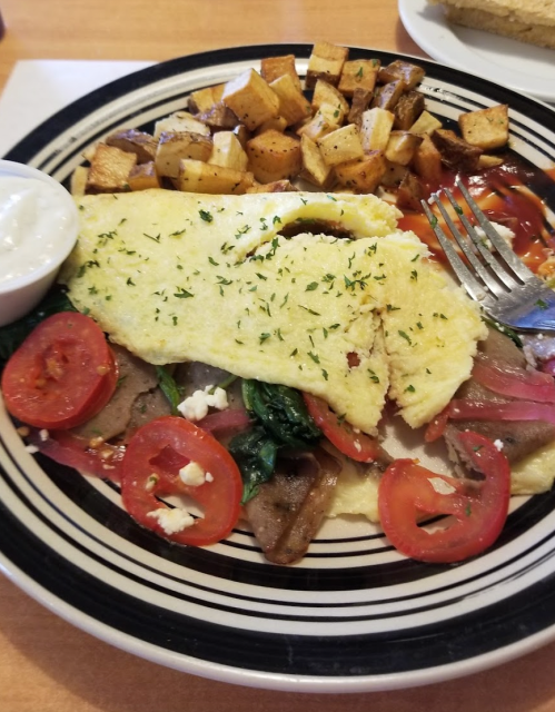 A plate of omelette with spinach, tomatoes, and feta, served with seasoned potatoes and a side of sour cream.