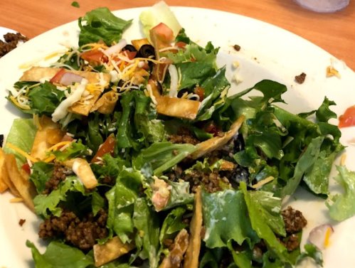 A plate of mixed salad with lettuce, tomatoes, cheese, black olives, tortilla strips, and ground beef.