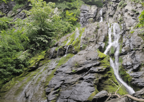 A lush green landscape featuring a rocky cliff with cascading waterfalls and moss-covered stones.