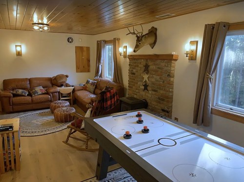 Cozy living room with leather sofas, a stone fireplace, and an air hockey table, featuring warm lighting and rustic decor.