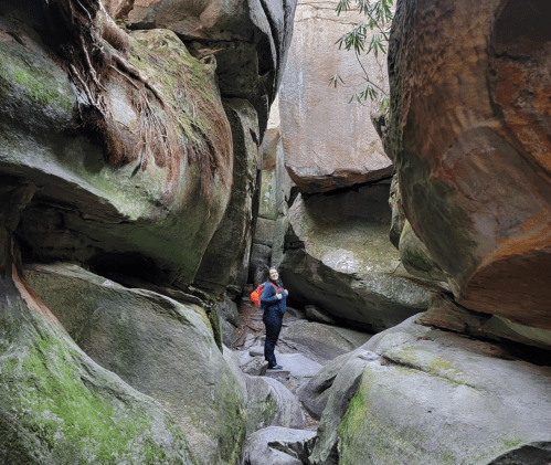 A person stands between large, moss-covered rock formations in a narrow canyon.
