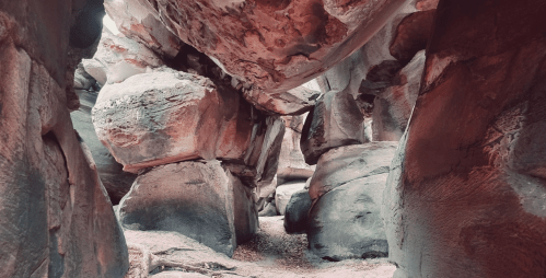 Narrow passage between large, textured rock formations in a canyon, with soft lighting highlighting the colors.