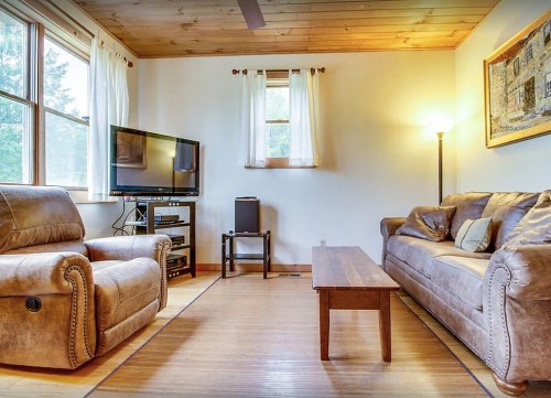 Cozy living room with a TV, two recliners, a sofa, and a wooden coffee table, illuminated by natural light.