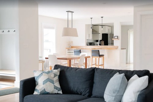 A modern living space featuring a dark sofa, dining area, and kitchen with light decor and wooden accents.