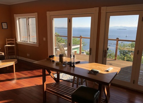 A cozy room with a wooden table, chairs, and large windows showcasing a scenic ocean view.