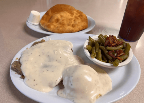 A plate of country-fried steak with gravy, green beans, and a biscuit, alongside a drink.