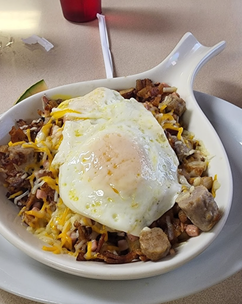 A dish of hash browns topped with cheese, meat, and a sunny-side-up egg, served in a white bowl.