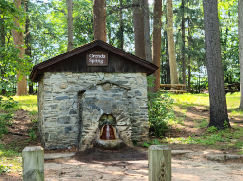 Stone structure labeled "Orenda Spring" with water flowing from it, surrounded by trees and greenery.