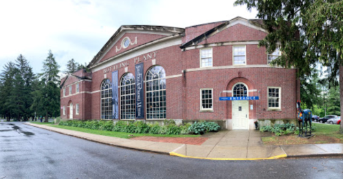 A brick building with large windows, surrounded by greenery, featuring a sign that reads "Building Plant."