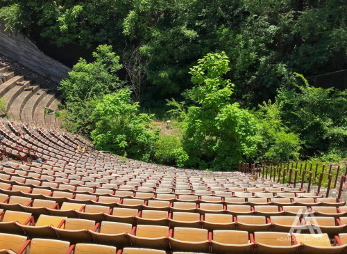 Abandoned outdoor amphitheater with overgrown vegetation and empty, worn seating.
