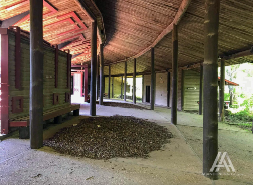 Interior of an abandoned building with wooden beams, a dirt floor, and a pile of leaves in the center.