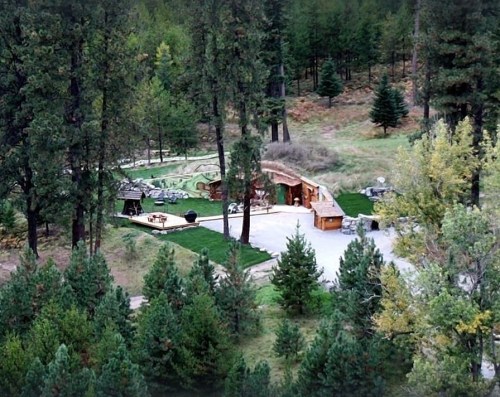 Aerial view of a secluded outdoor area with a stone structure, picnic tables, and surrounded by trees.