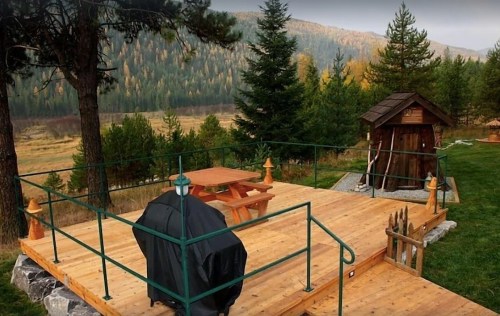 A wooden deck with a picnic table and grill, surrounded by trees and mountains in a serene outdoor setting.