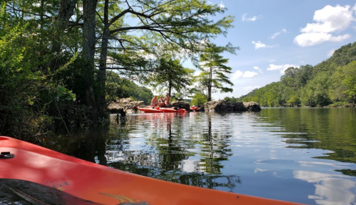 A serene lake scene with kayakers enjoying a sunny day surrounded by trees and rocky outcrops.