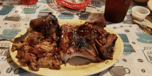 A plate of barbecue featuring pulled pork, brisket, and a side of sauce, set on a patterned tablecloth.