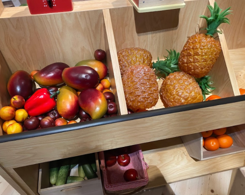 A wooden display with colorful artificial fruits, including mangoes, pineapples, peppers, and oranges.