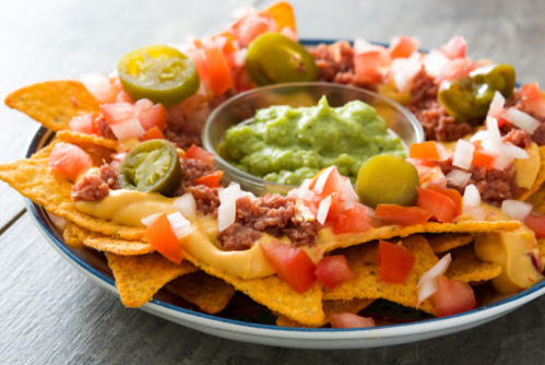 A plate of nachos topped with cheese, ground meat, tomatoes, onions, jalapeños, and a side of guacamole.