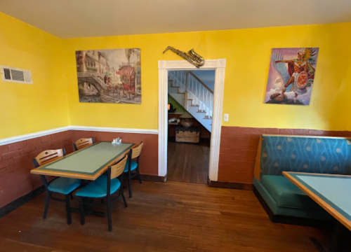 Cozy restaurant interior with yellow walls, tables, and colorful artwork, featuring a saxophone above the doorway.