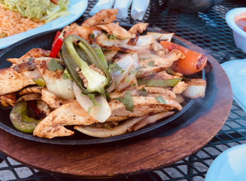 Sizzling fajitas with grilled chicken, peppers, and onions on a wooden platter, with steam rising.