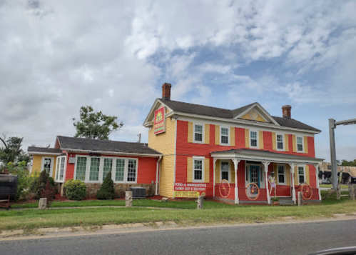 A colorful two-story restaurant with yellow and red siding, surrounded by greenery and a cloudy sky.