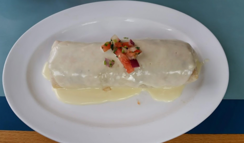 A large burrito topped with melted cheese and fresh pico de gallo, served on a white plate.