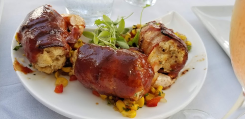 Three stuffed sausages on a white plate, garnished with greens and served on a bed of corn and diced vegetables.