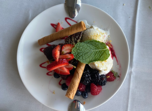 A dessert plate featuring chocolate cake, berries, ice cream, and decorative mint leaves, garnished with wafer sticks.
