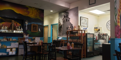 Interior of a colorful restaurant featuring murals, tables, and a visible kitchen area with various condiments.