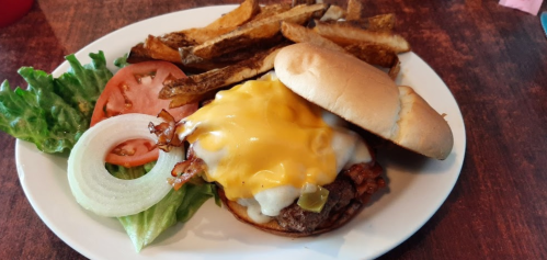 A cheeseburger topped with bacon and melted cheese, served with lettuce, tomato, onion, and a side of fries.