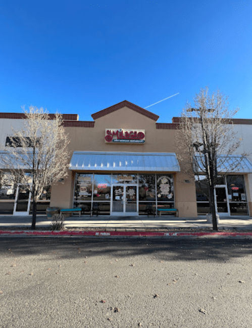 Front view of a restaurant with a sign, large windows, and trees in front, under a clear blue sky.
